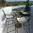 Brass cocktail table with black marble top paired with black wire chairs on a bright balcony overlooking trees and distant city skyline