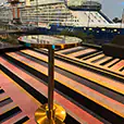 Brass cocktail table with black top positioned in a modern interior space overlooking a harbour with a large cruise ship visible through floor-to-ceiling windows