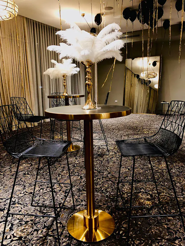 Brass cocktail tables with black tops arranged in a lounge-style event space with upholstered seating, wall lighting and decorative interior finishes