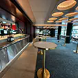 Brass cocktail tables with white tops arranged throughout a modern bar venue interior with marble bar counter, shelving, and ambient ceiling lighting