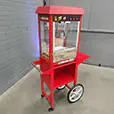 Classic red popcorn machine cart with glass display cabinet and wheeled snack station setup for events and functions