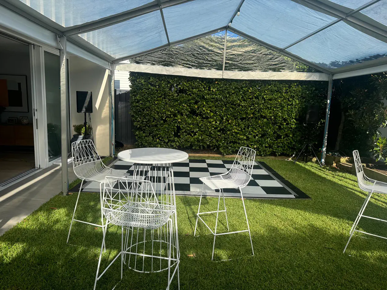 Clear marquee with transparent roof panels set up over grass with white wire chairs, cocktail table and a black and white dance floor area