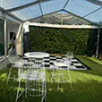 Clear marquee with transparent roof panels set up over grass with white wire chairs, cocktail table and a black and white dance floor area