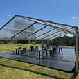 Clear roof marquee set up on grass with black flooring, festoon lighting and bar tables arranged for an outdoor event in a rural setting