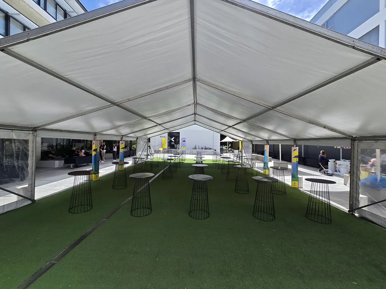 Clear span marquee structure with multiple cocktail tables arranged on artificial grass for an outdoor event setup