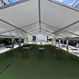 Clear span marquee structure with multiple cocktail tables arranged on artificial grass for an outdoor event setup