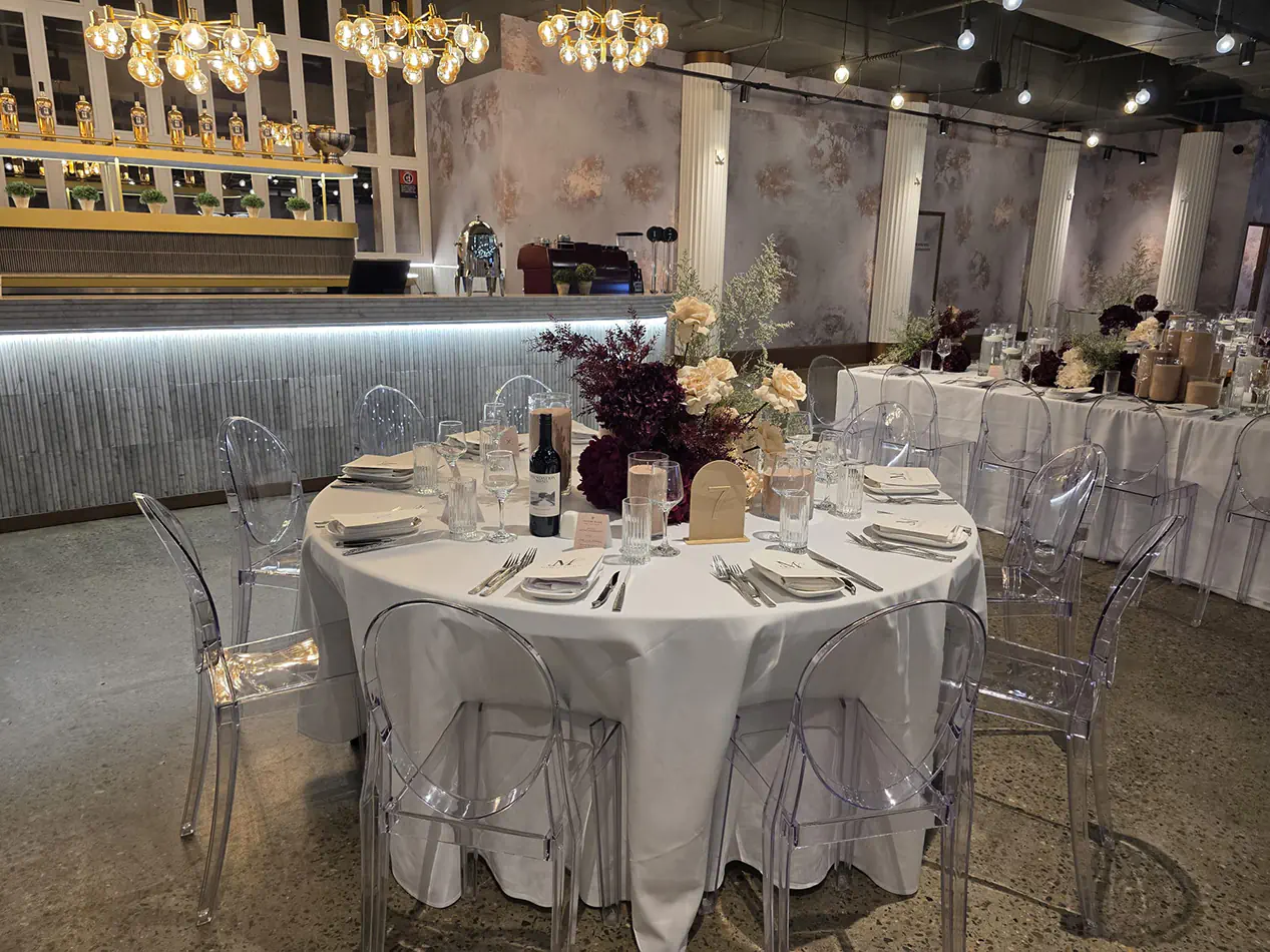 Elegant wedding reception table setting with clear Victorian chairs, white table linen, floral centrepieces and ambient chandelier lighting