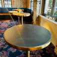A gold-based round table with a brass cocktail bar design and a black marble top in a room.