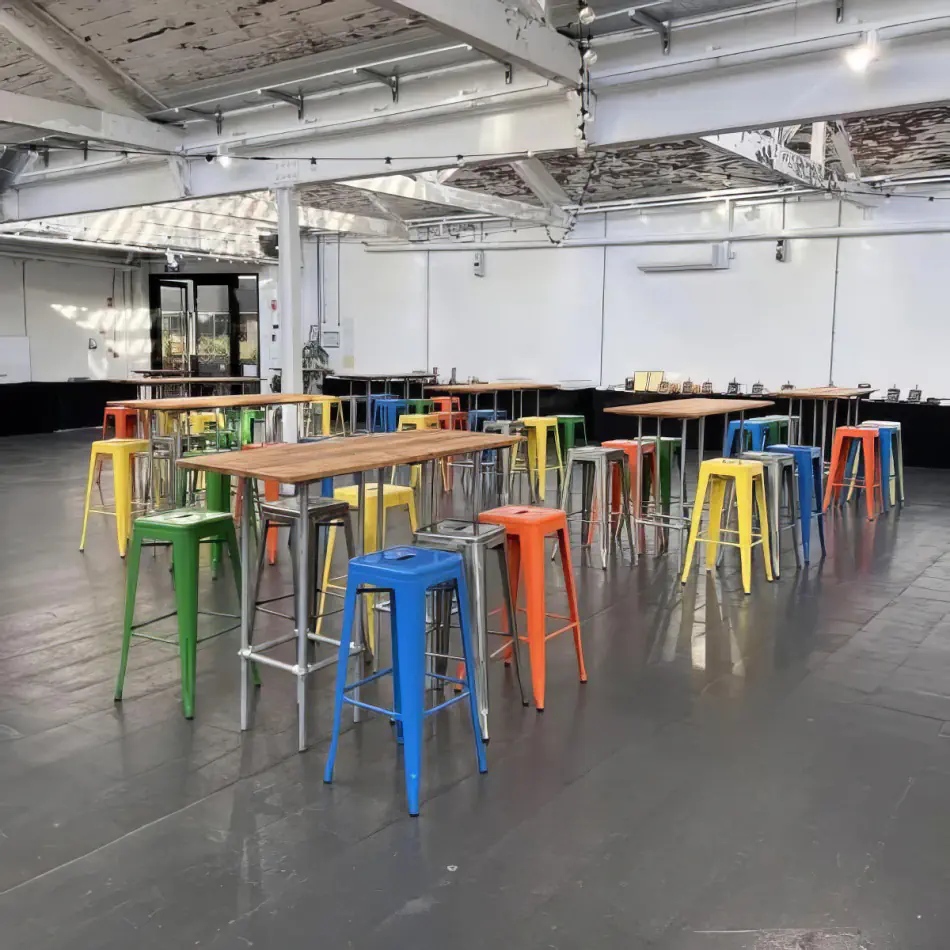 Assorted tolix stools in blue, yellow, green and red paired with timber high bar tables in an industrial-style event space with polished concrete floors