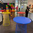 Colourful wire cocktail tables in blue, yellow and red arranged for a vibrant indoor party setup with decorative balloons and event styling