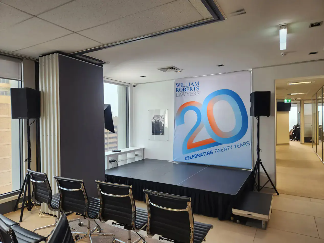 Conference stage setup with raised platform, speakers on stands, branded backdrop, and seating area in corporate office environment for presentation or event