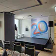 Conference stage setup with raised platform, speakers on stands, branded backdrop, and seating area in corporate office environment for presentation or event