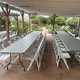 Covered patio event setup with grey plastic trestle tables and white folding chairs arranged for a garden gathering