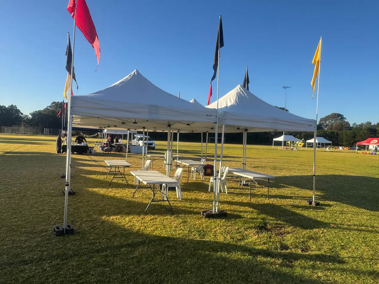 Double white pop-up marquee setup with tables and seating arranged on a sports field for a community gathering