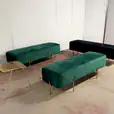 Three emerald green and gold ottoman benches in a room.