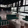 Emerald green velvet lounge seating with white wire frame furniture and ottoman stools inside a waterfront event venue with floor-to-ceiling windows