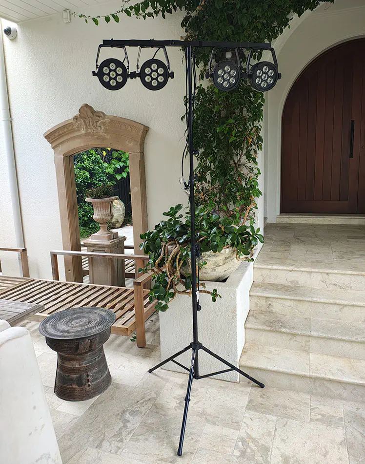 Portable event lighting stand with multiple LED stage lights set up outdoors near a patio area with plants, stone flooring and decorative mirror