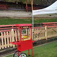 Popcorn machine cart in bright red set up under outdoor canopy tents alongside fencing and event equipment