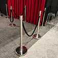 Event queue barriers with chrome stanchions and black ropes set in front of a red curtain backdrop on carpeted floor