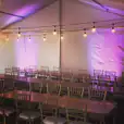 A tent with tables and chairs set up with purple festoon lighting.