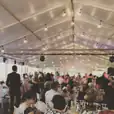 A group of people sitting at tables in a tent adorned with Festoon Light Hire.