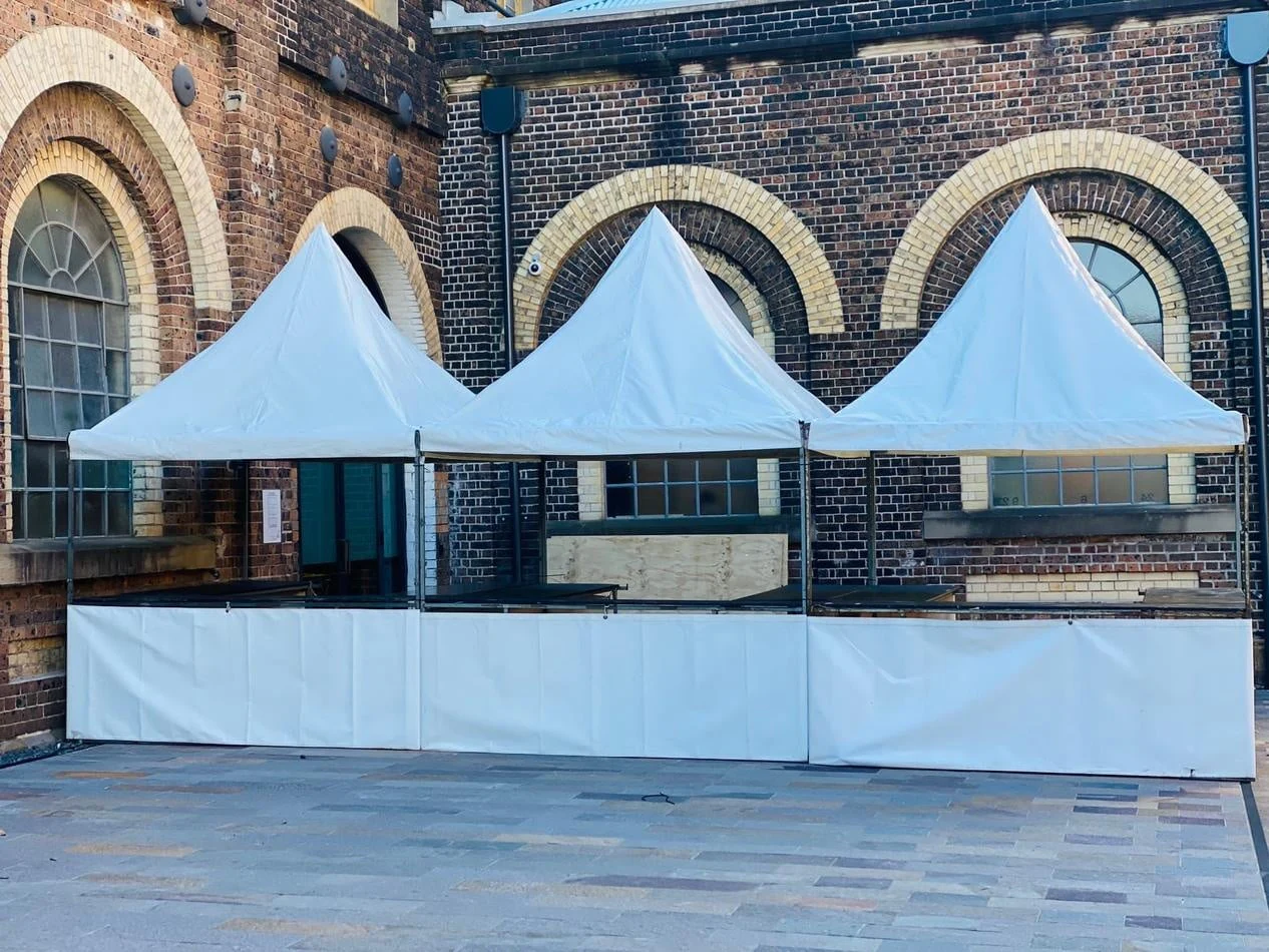 Three white tents set up in front of a brick building, available for fete stall/tent hire (including setup).