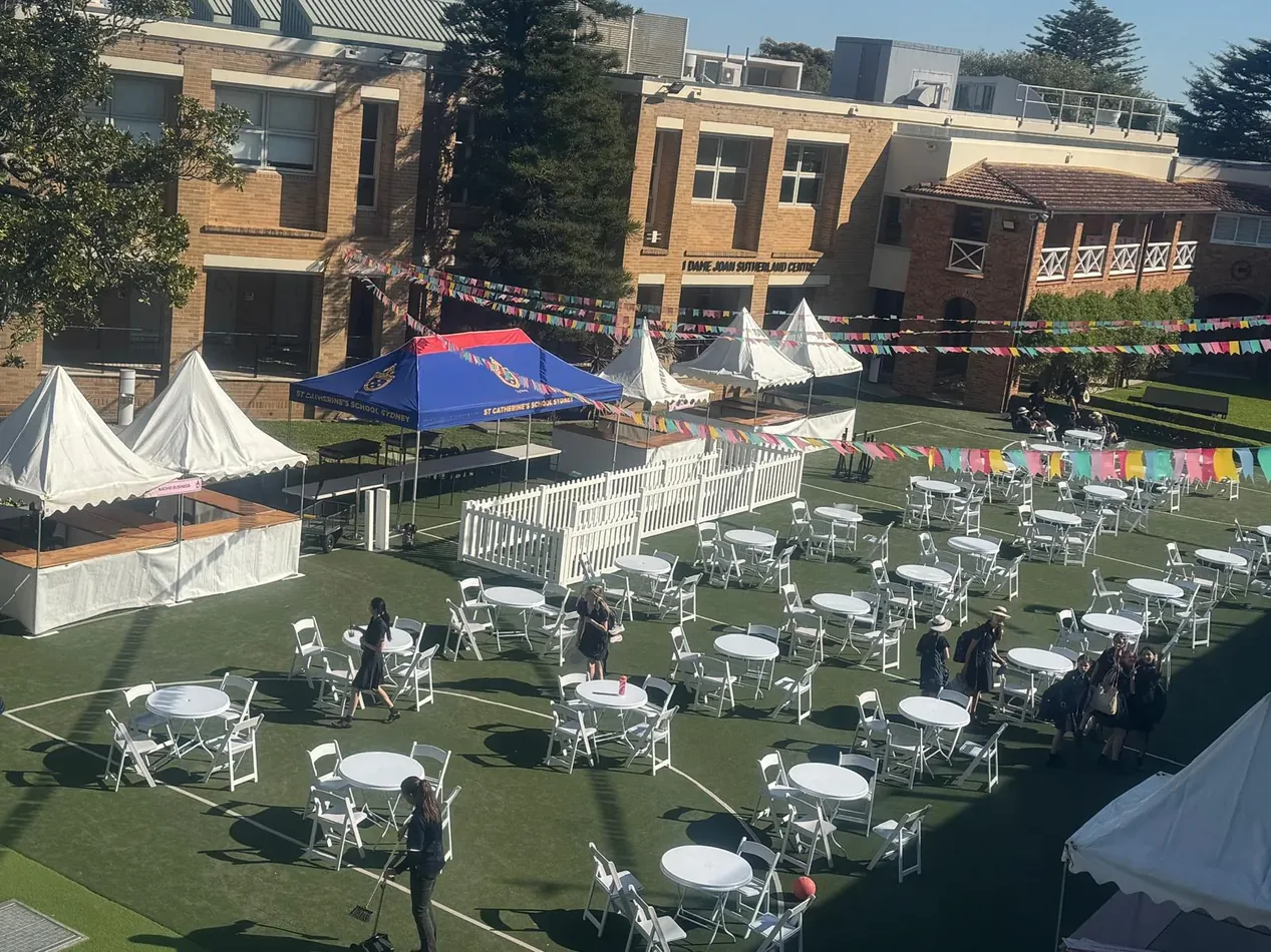 Fete stalls with cafe tables and white plastic chairs at an outdoor community event