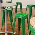 Forest green Tolix stools arranged around round stainless steel café tables in an indoor event setup