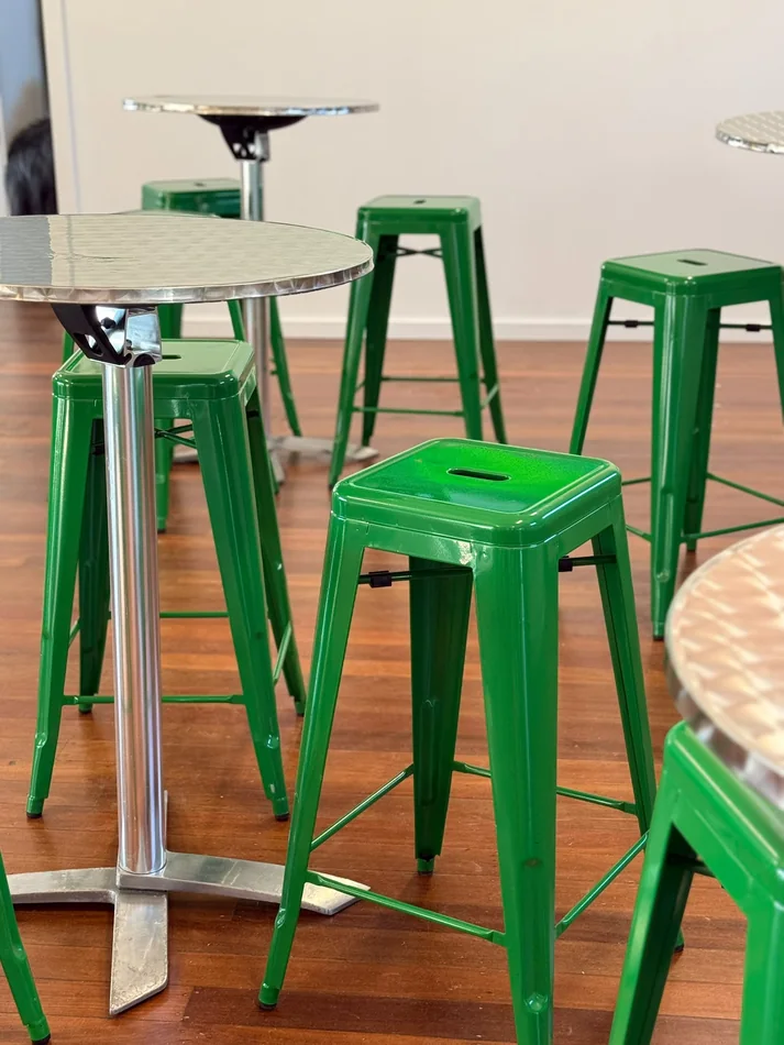 Forest green Tolix stools arranged around round stainless steel café tables in an indoor event setup