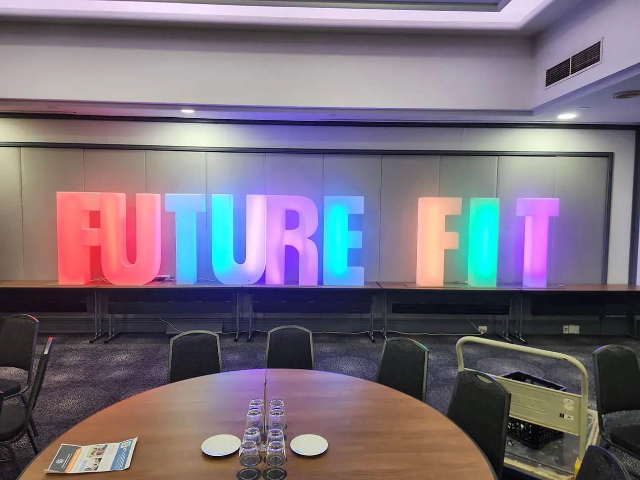 Large FUTURE FIT illuminated event letters with multicoloured LED lighting at an indoor conference venue