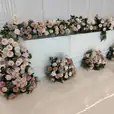 Gloss bridal table decorated with cascading ivory, blush, and champagne-toned floral arrangements, styled against a white backdrop for a wedding reception.
