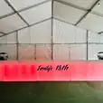 A large tent with a bar in the middle of it, featuring a dazzling Glow Corner Bar.