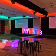 A conference room with colorful stools, a projection screen, and Glow Cube Hire for added vibrancy.