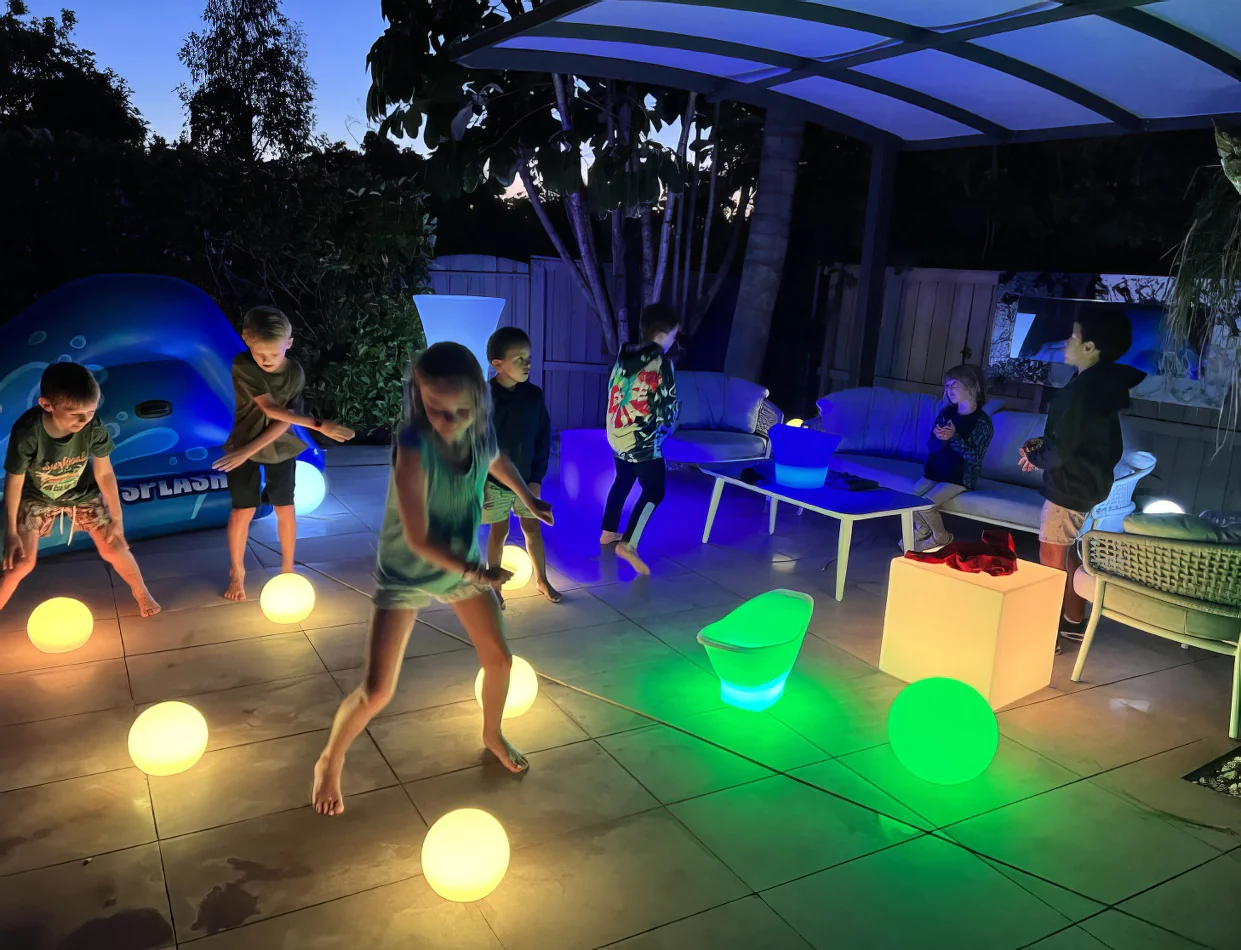 Kids playing with glowing balls in a backyard rented from Glow Sphere Hire - 20cm.