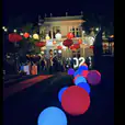 A group of people are walking down a street at night, carrying a mesmerizing 60cm Glow Sphere Hire.