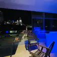 A balcony with a straight bar hire and a view of the city, illuminated by blue lights.