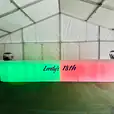 A straight LED bar in a tent, emitting a vibrant display of green, red, and blue glow.