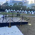 Gold bollards with black velvet ropes surrounding an outdoor event platform and entry walkway