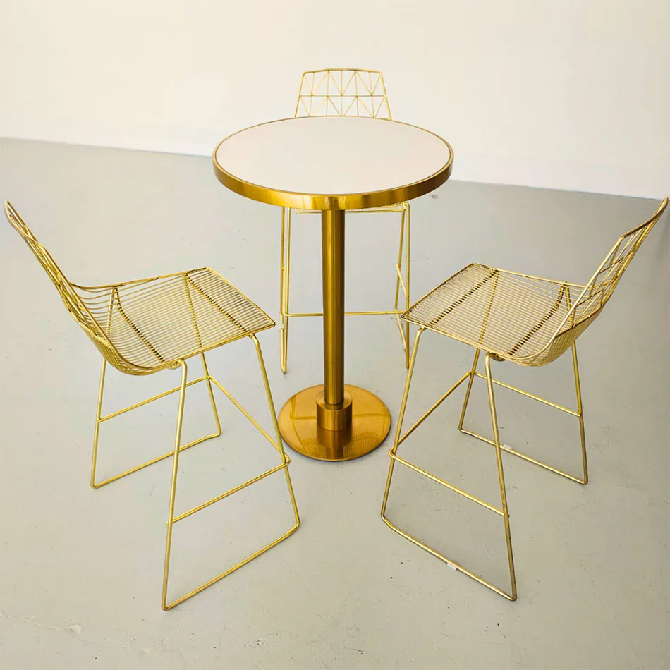 Stylish gold cocktail table with white top, paired with matching gold wire chairs in a contemporary setting.