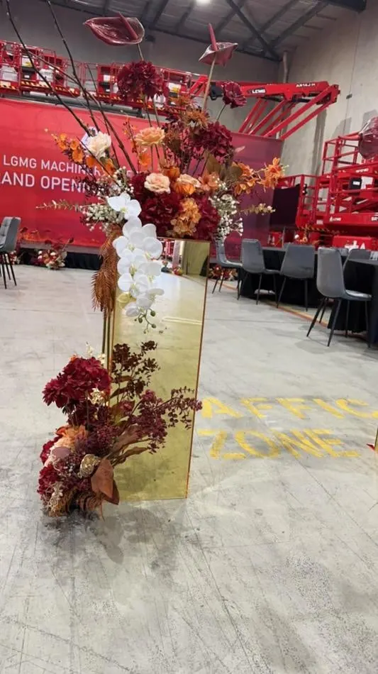 A red and gold flower arrangement in a warehouse with a gold mirror plinth.
