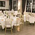 A room with tables and chairs set up for a wedding reception, featuring elegant Gold Tiffany Chair Hire.