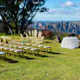 A wedding ceremony set up in a grassy area with mountains in the background, featuring Gold Tiffany Chair Hire.