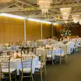 A large hall with tables and chairs set up for a wedding reception, featuring elegant gold Tiffany chair hire.