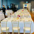 A spacious room with tables and Gold Tiffany chairs set up.