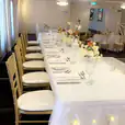 A table set up for a wedding with white linens and Gold Tiffany Chair Hire, adorned with lights.