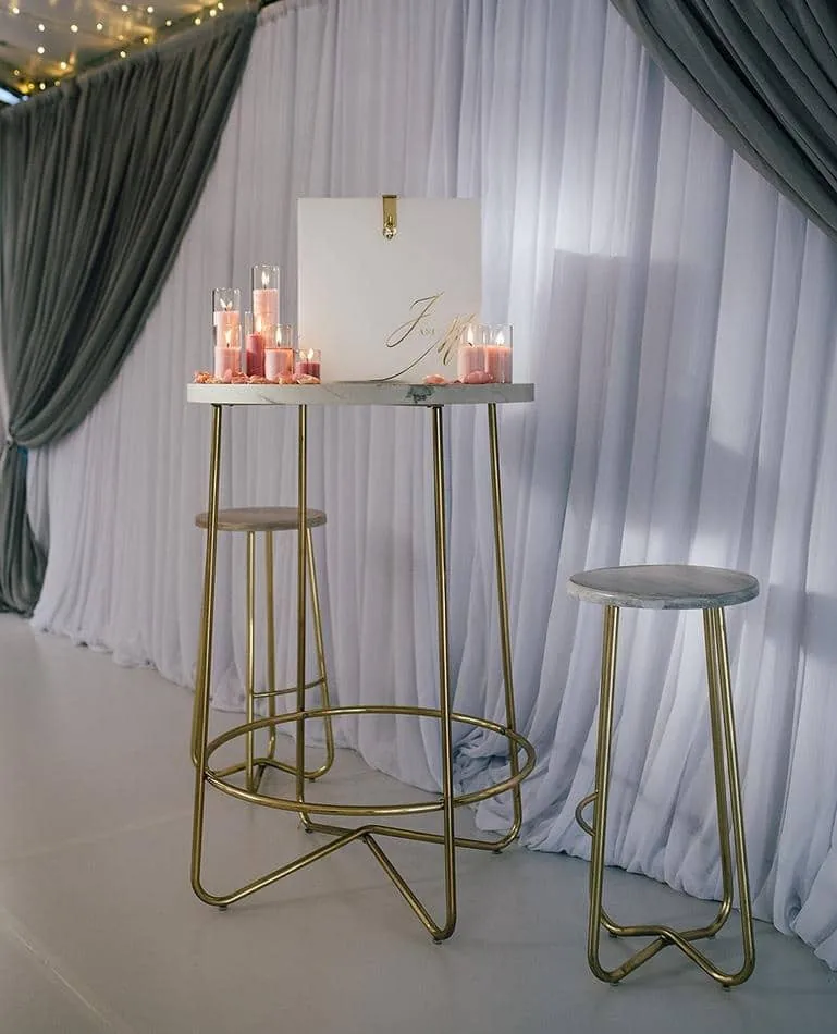 A gold table with candles and stools in front of a curtain, available for hire.