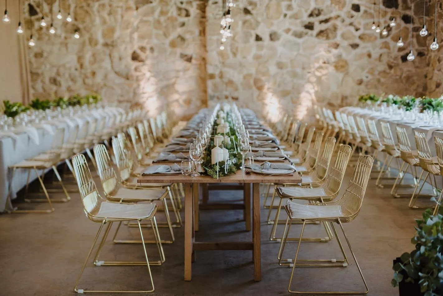 A wedding reception set up in a stone barn with gold wire chairs.