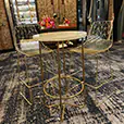 Gold wire cocktail table with marble top paired with matching gold wire stools in an indoor event space with exposed brick walls and patterned carpet