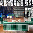 Green velvet wire lounge furniture with white ottoman stools and round coffee tables inside a timber-clad harbourfront function venue