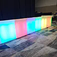 Illuminated glow bar with colour changing LED panels set up beside a stage curtain at an event venue